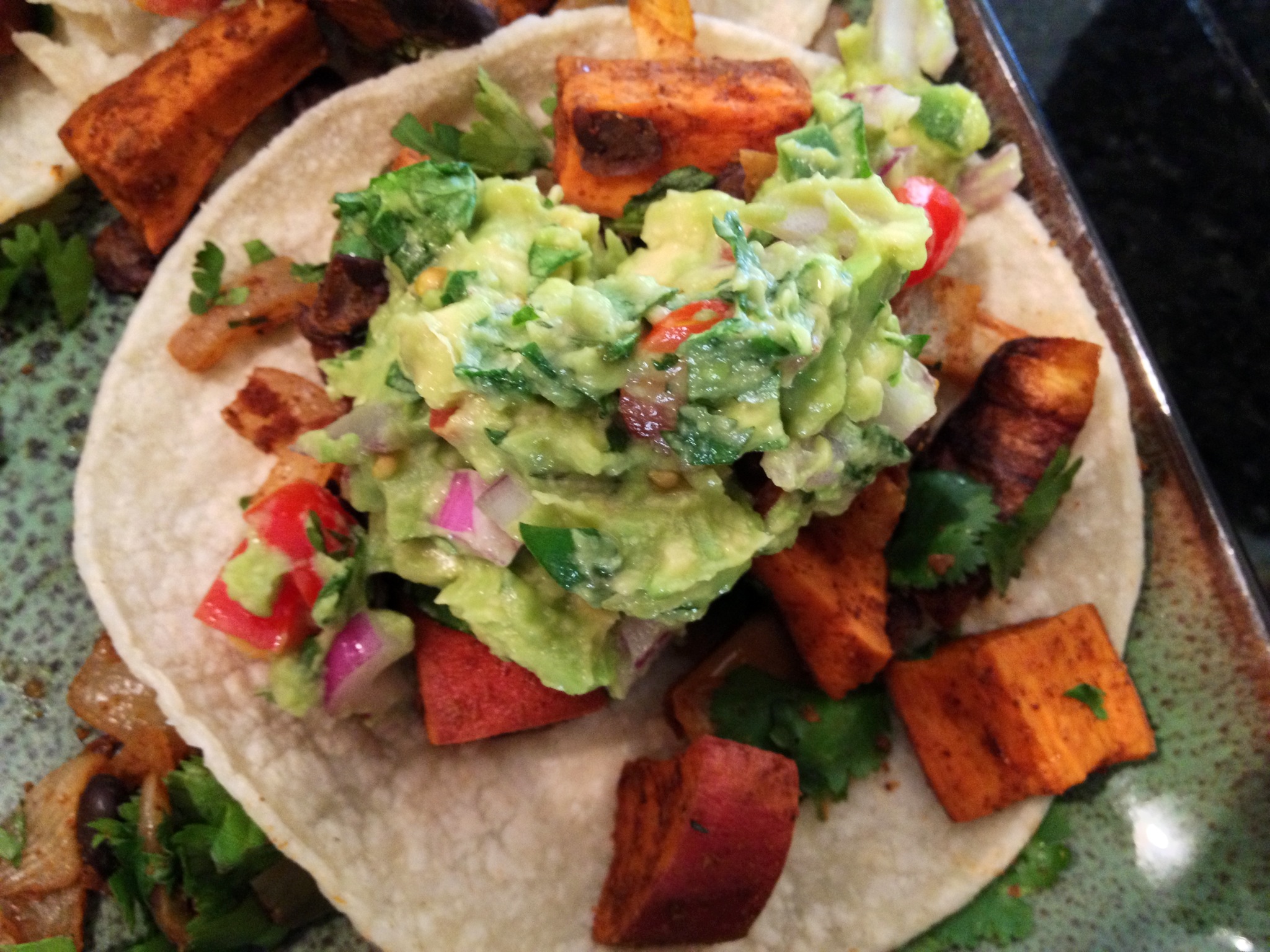 A Tortilla with roasted sweet potatoes and guacamole on it