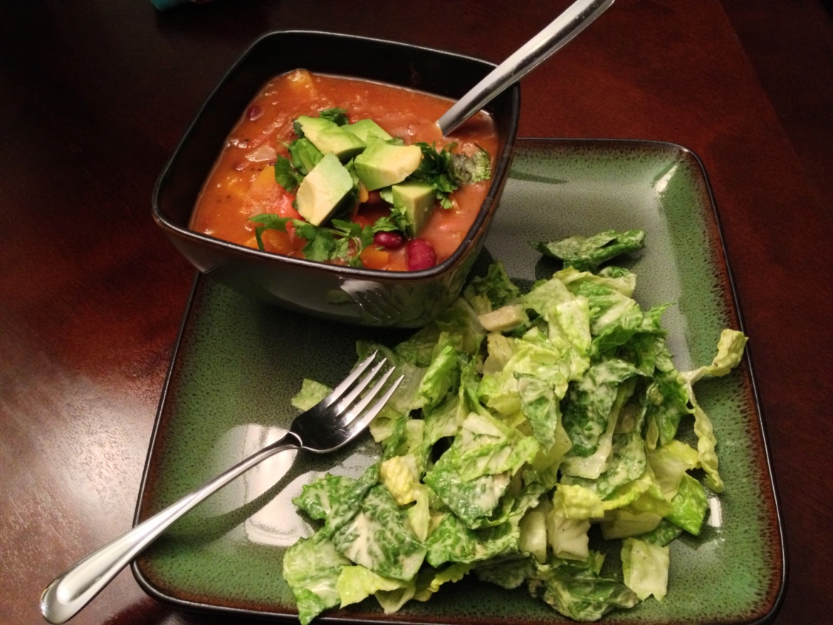A bowl of butternut squash soup and vegan Caesar salad on a square plate