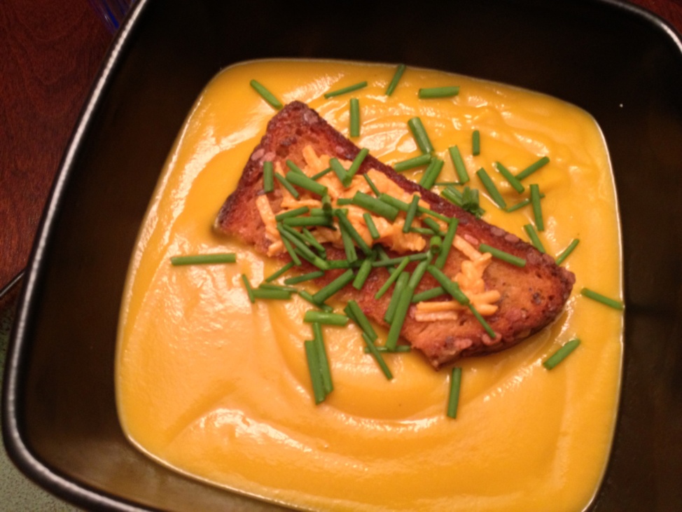 Creamy acorn squash soup with cheesy croutons in a black square bowl