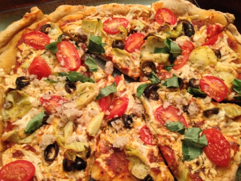 Vegan, gluten-free sliced pizza pie with cherry tomatoes, artichokes, olives, and basil