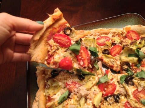 Vegan sliced pizza pie with cherry tomatoes, artichokes, olives, and basil