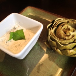 A steamed artichoke and a ramekin with aioli on a plate