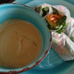 A bowl with peanut butter sauce and two fresh rolls