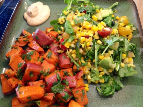Roasted chopped sweet potatoes and a salad with corn and greens on a plate