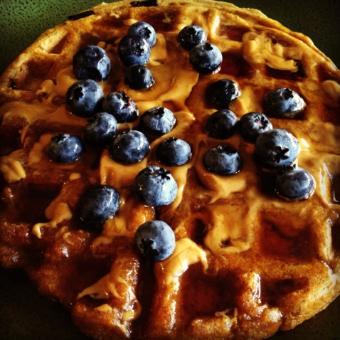 A pumpkin spiced waffle coated with maple syrup and topped with fresh blueberries