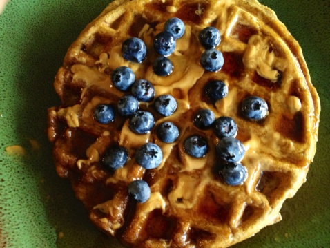 A pumpkin spiced waffle with maple syrup and fresh blueberries