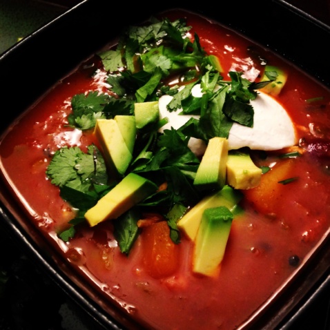 A bowl of red soup topped with avocado and cilantro