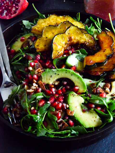 Carmelized Squash salad with greens and pomegranate vinaigrette in a black bowl