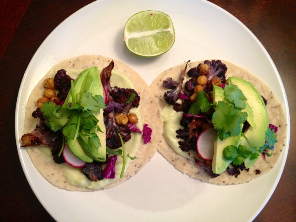 Two tacos with cauliflower, chickpeas, avocado, and cilantro on a plate