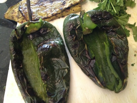 Two grilled poblano peppers on a cutting board