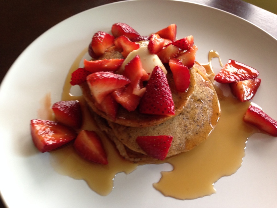 Lemon poppy seed pancakes with syrup and strawberries on a white plate