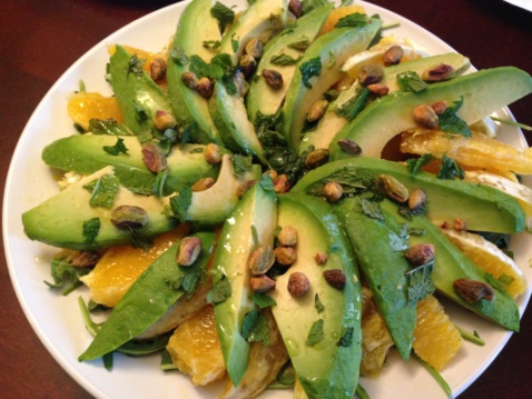 Sliced avocado, oranges, arugula, and pistachios on a white plate