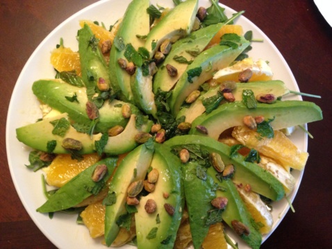 A salad of sliced avocado, oranges, arugula, and pistachios