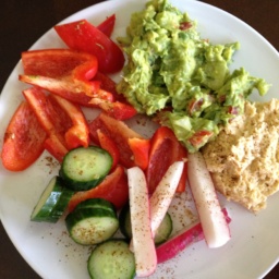 Hummus, guacamole, and sliced fresh vegetables on a white plate