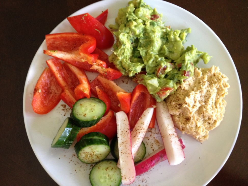 Hummus, guacamole, and sliced fresh vegetables on a white plate