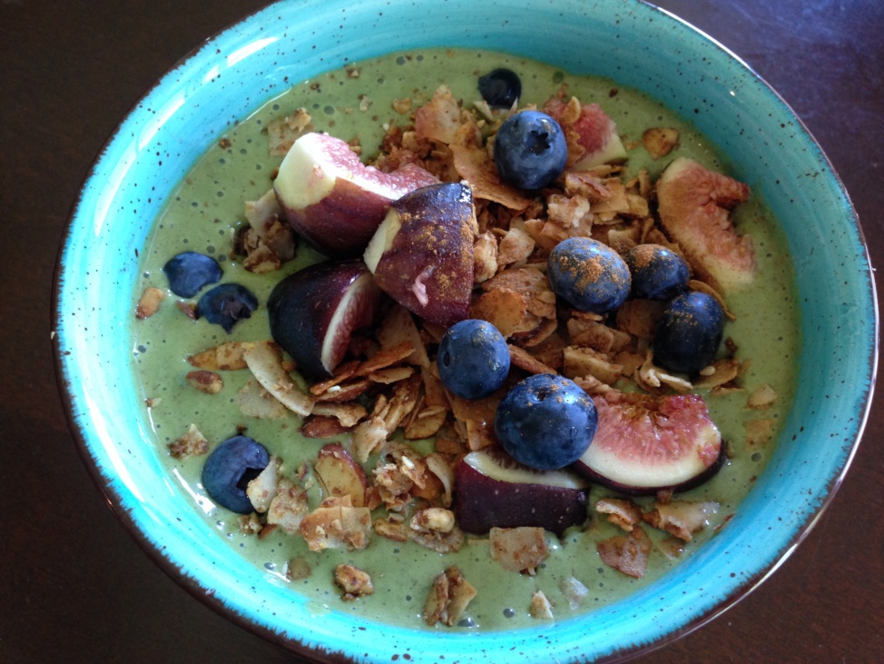 A green smoothie topped with granola, fresh figs, and blueberries