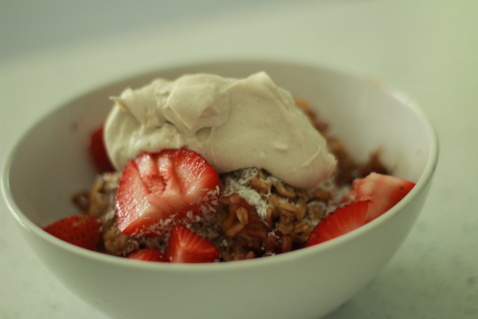 Strawberry rhubarb baked oatmeal with coconut whipped cream in a white bowl