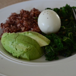 Avocado, kale, rice and a hard boiled egg on a white plate